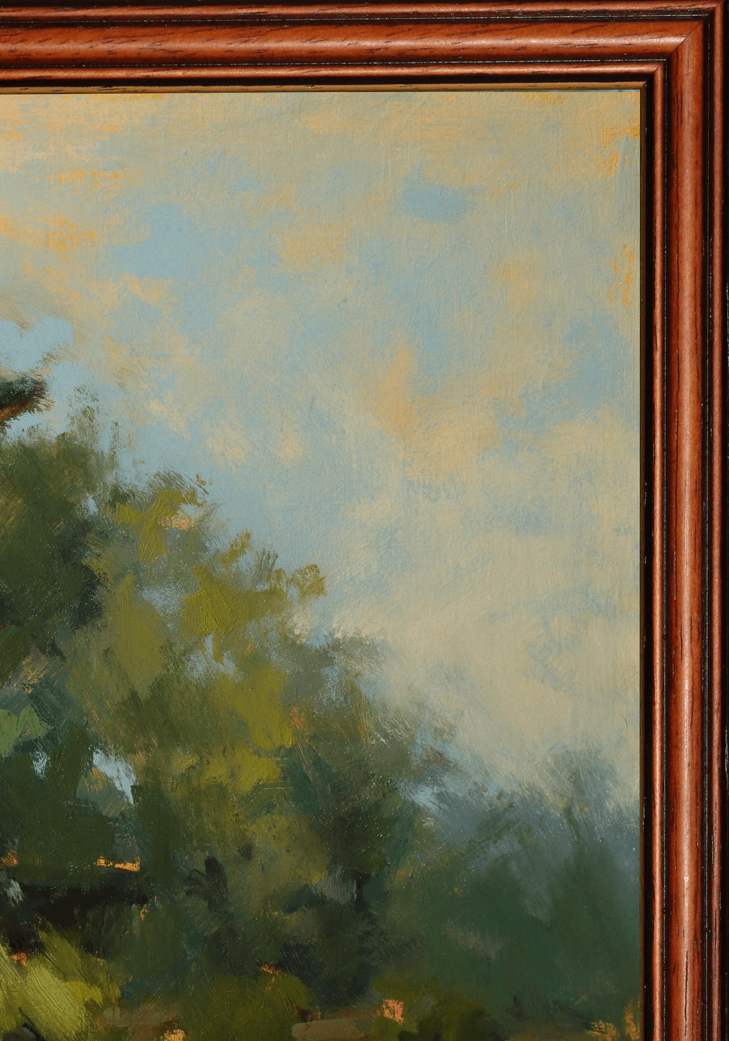 Close-up of a framed landscape painting showing green trees and foliage under a soft blue and yellow sky, with a reddish-brown wooden frame visible on the left and right edges.
