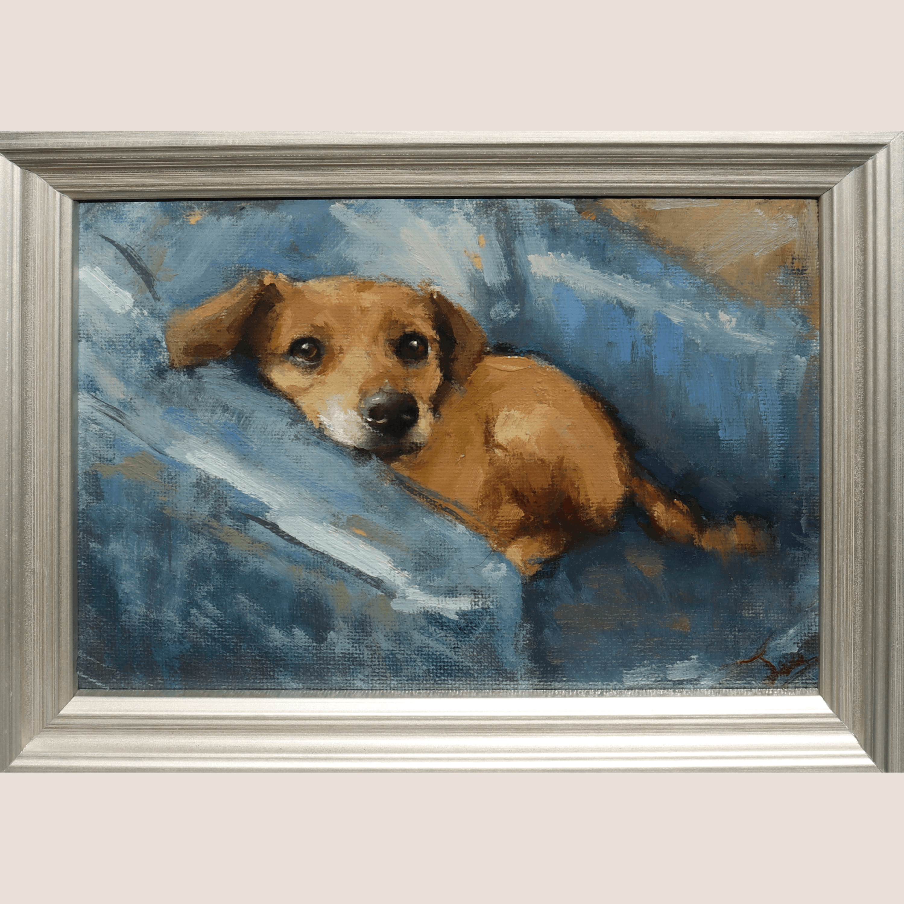 A framed painting of a small brown dog resting on a blue couch, shown against a light beige wall. The artwork has an expressive brushstroke style, and the piece is enclosed in a wide, textured silver frame.