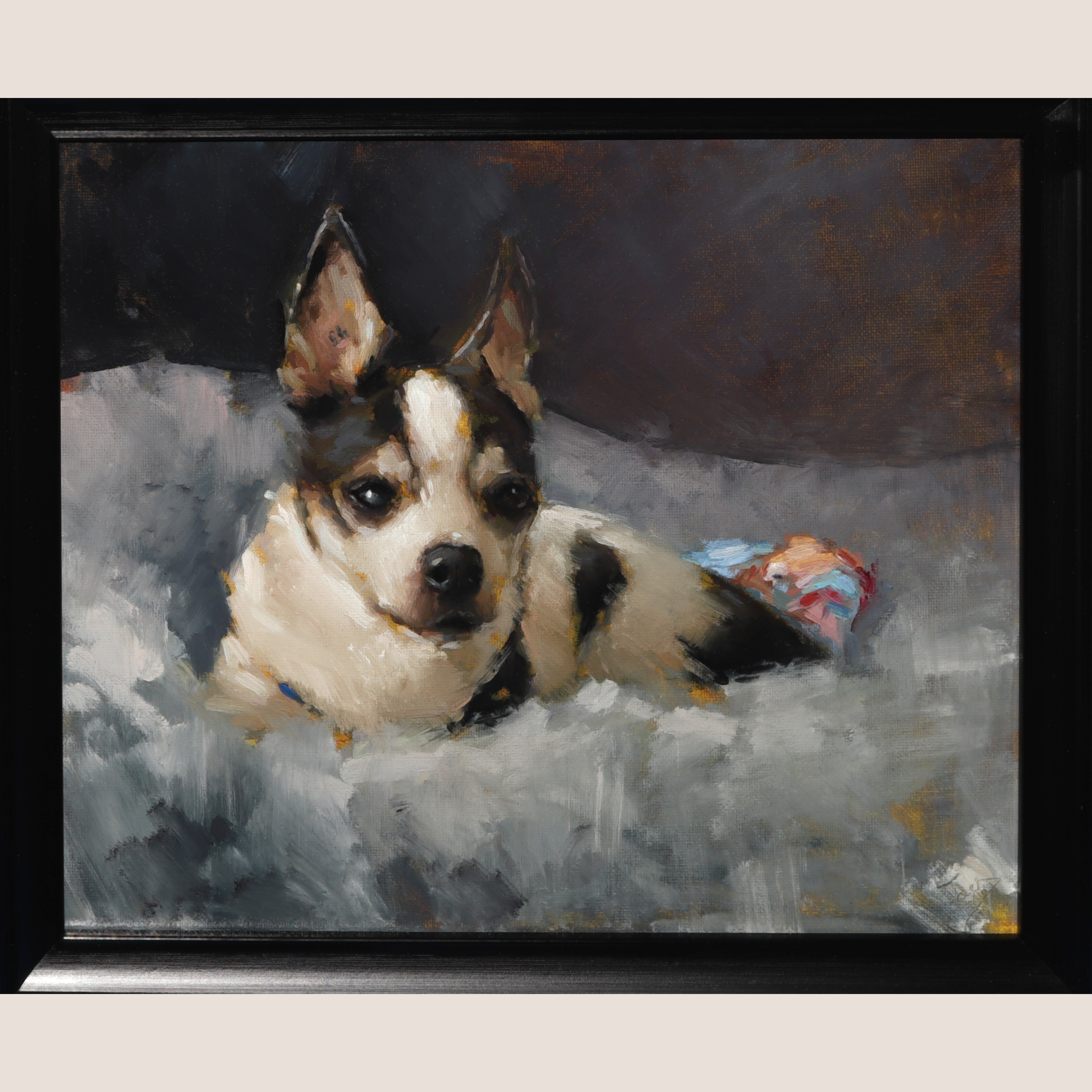 A framed portrait painting of a black and white dog lying on a gray blanket, with a dark background and a small colorful cloth near the dog's side. The artwork is shown in a black frame against a light neutral background.