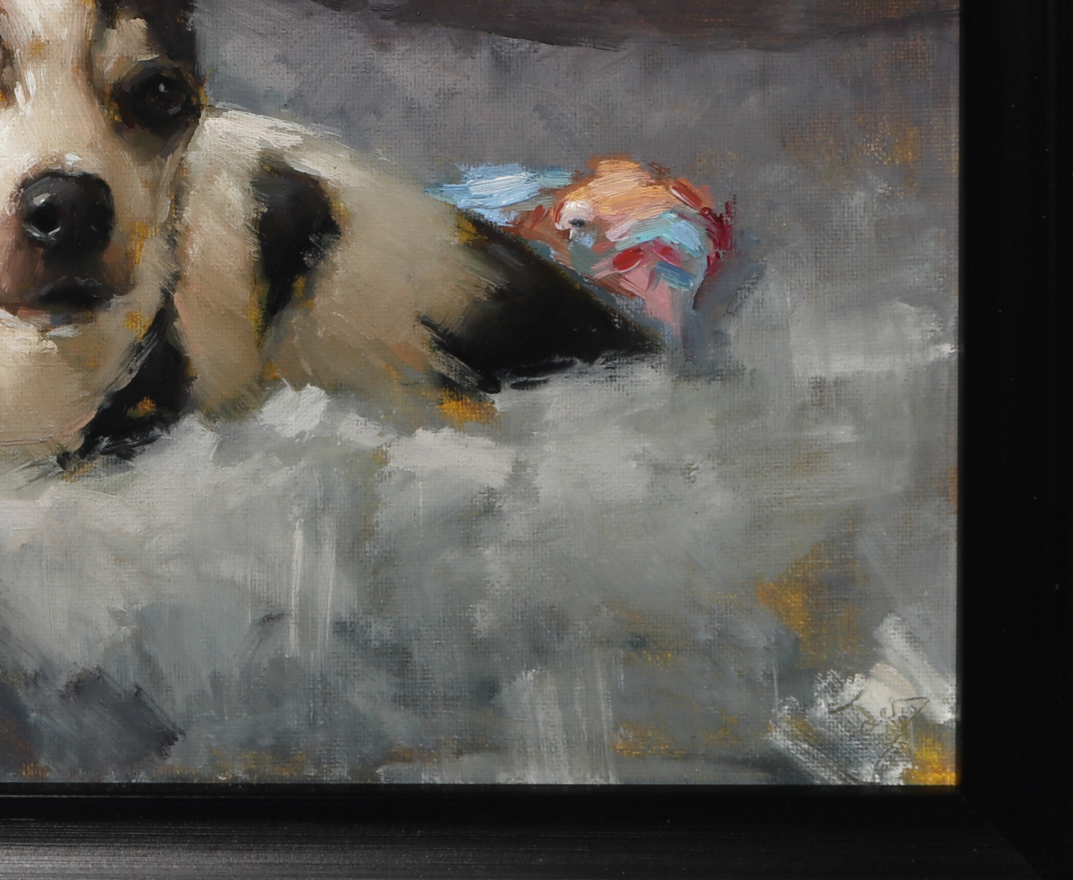 A close-up of a framed painting depicting a black and white dog resting on a gray and white textured surface, with a small colorful object in the background.