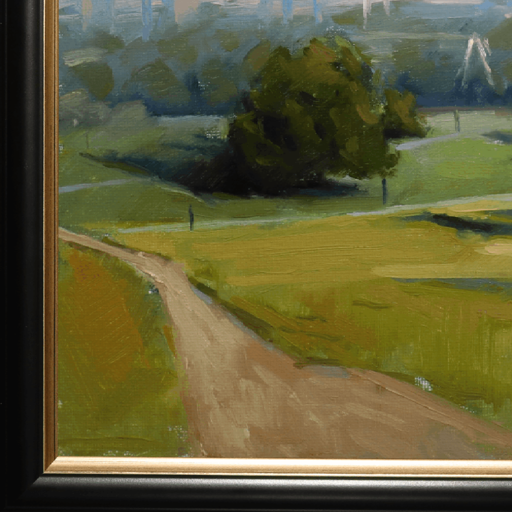Close-up of a framed landscape painting showing a dirt path winding through green fields toward a dark green tree, with visible black and gold frame edges.