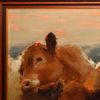 Close-up of a framed painting showing the head of a brown cow against a soft beige and orange sky, with visible brushstrokes and a dark wood frame.